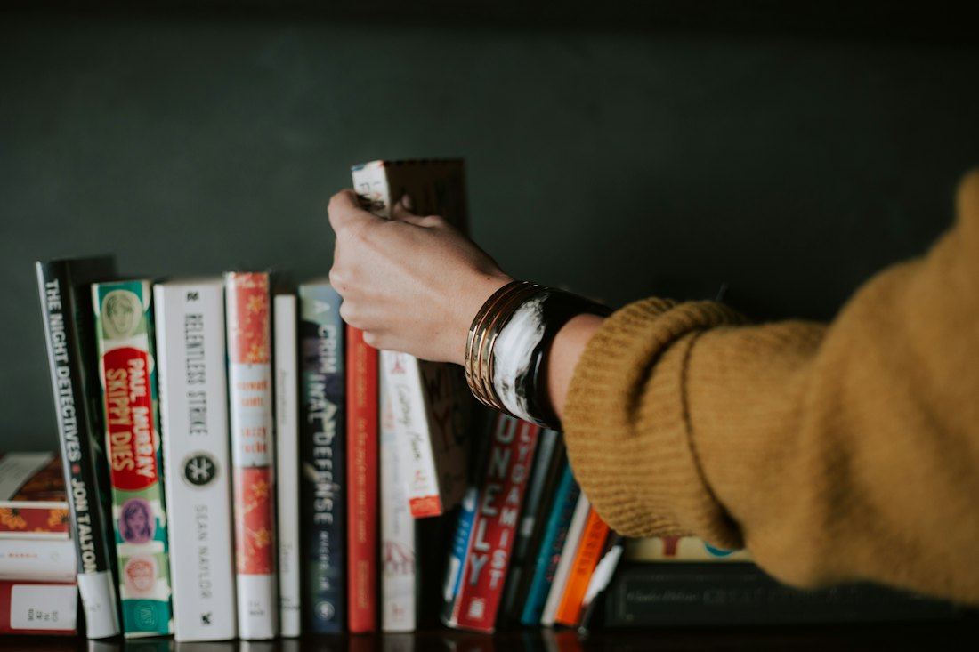 A reader pulling a paperback from a tightly packed shelf